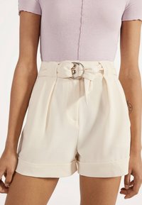 Krémově barevné kraťasy s vysokým pasem, záhyby a páskem s kulatou stříbrnou sponou. Hladká látka s obrácenými lemy.
