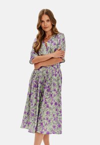 Kvetinové šaty s ľahkou zelenou látkou a fialovými kvetinovými vzormi, krátkymi rukávmi, výstrihom do V a splývavým strihom A-line.