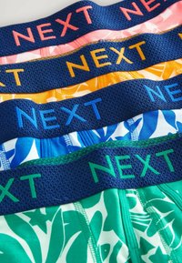 Quatre paires de maillots de bain avec des motifs colorés. Dotés d'une ceinture élastique texturée avec la marque "NEXT" en couleurs contrastées.