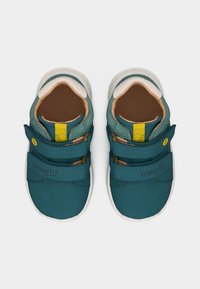 Ζευγάρι παιδικά αθλητικά παπούτσια σε τιρκουάζ με διπλές λουρίδες Velcro, λευκές σόλες και κίτρινη θηλιά στο γλώσσα, φαίνεται από πάνω.