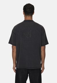 T-shirt oversize grigio scuro in cotone con maniche corte. Presenta una stampa rialzata nera di una farfalla e del testo sul retro.