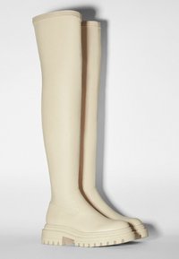 Botas altas hasta la rodilla de color beige con un acabado liso y mate, suela gruesa de color claro, puntera redondeada y lados elásticos para un fácil calzado.