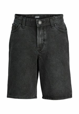 Fiú fehér rövid ujjú inget visel fehér póló fölött, fekete rövidnadrágot, fehér zoknit, sportcipőt és zöld baseballsapkát, fehér háttér előtt áll.