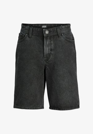 Fiú fehér rövid ujjú inget visel fehér póló fölött, fekete rövidnadrágot, fehér zoknit, sportcipőt és zöld baseballsapkát, fehér háttér előtt áll.