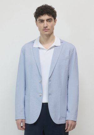 Light blue blazer in textured fabric, featuring a single-button closure, two front pockets, and a notched collar, worn over a white shirt.
