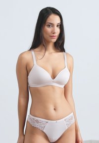 Jasnoróżowy bezprzewodowy biustonosz o gładkim wykończeniu i regulowanych ramiączkach, dopasowany do niego komplet majtek z koronkowym wykończeniem po bokach.