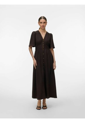 Kvinde med brunt hår samlet i en lav hestehale iført en mørkebrun midi-kjole med knapper, korte puffærmer og sorte sandaler med remme.