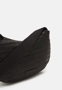 Borsa nera intrecciata con una forma curvata, caratterizzata da una superficie testurizzata, una morbida tracolla nera e un'etichetta sul lato.