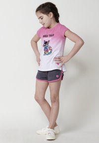 Camiseta de manga corta en degradado rosa y blanco con un gráfico de gato brillante, combinada con pantalones cortos grises con ribetes rosas y acentos de corazón.