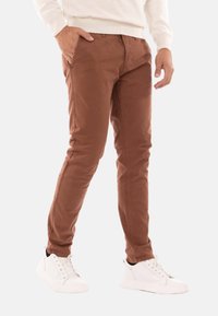 Pantaloni in cotone marrone a taglio slim, caratterizzati da tasche anteriori e una texture morbida, abbinati a sneakers bianche.