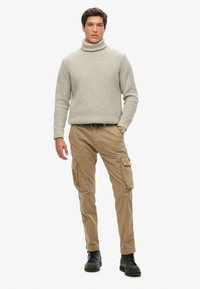 Lys grå strikket pologenser, beige cargo-bukser med lommer og sorte snørebåndssko. Udendørs casual tøj, tilpasset pasform.