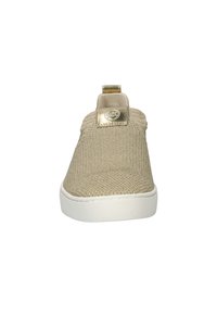 Scarpa slip-on in maglia beige con suola bianca, caratterizzata da un dettaglio metallico oro sul retro e un logo. Tessuto dalla superficie liscia.