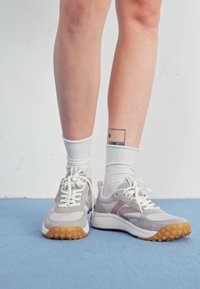 Szare i białe sneakersy z różowymi akcentami, perforowaną fakturą i gumowymi podeszwami z małymi okrągłymi uchwytami, sznurowane białymi sznurówkami.