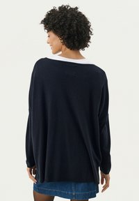 Maglione oversize blu scuro con vestibilità rilassata, scollatura ampia e maniche lunghe. Presenta un tessuto morbido e texture e un colletto bianco a strati.
