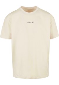 Cremefarvet bomulds T-shirt med rund hals og korte ærmer, med et lille sort "MERCHCODE" logo på forsiden.