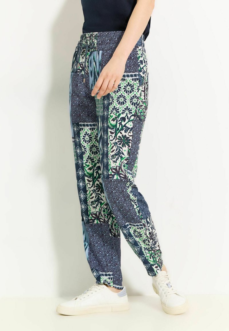 Joggers à motifs présentant un mélange de designs floraux verts et bleus, une taille élastique avec cordon de serrage, et un tissu doux.