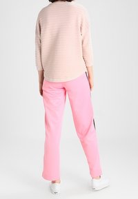 Helles rosa strukturiertes Langarmoberteil mit Rundhalsausschnitt, kombiniert mit rosa Sporthosen mit schwarzen seitlichen Streifen und weißen Sneakers.