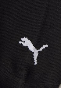 Mustmust kangas tekstuuriga viimistlusega, millel on valge Puma logo, veidi tõstetud ja kudumisega materjali sisse, et lisada detaili.