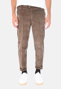 Pantaloni in vellutino marrone con righe verticali, vestibilità slim, risvolti, indossati con sneakers bianche. Design minimalista, senza marchi visibili.