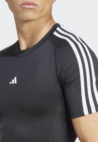 Zwarte sportshirt met witte drie-strepen accenten op de schouders, een ronde halslijn en een aansluitend ontwerp met een soepele textuur.