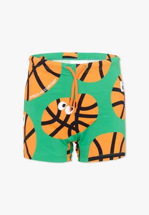 Maillot de bain vert avec un motif de ballons de basketball orange avec des yeux, cordon orange et texte blanc « Stella McCartney » sur le côté gauche.