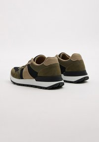Zapatillas deportivas que combinan malla negra, ante verde olivo y detalles en beige. Suela de goma gruesa con textura para ofrecer agarre.