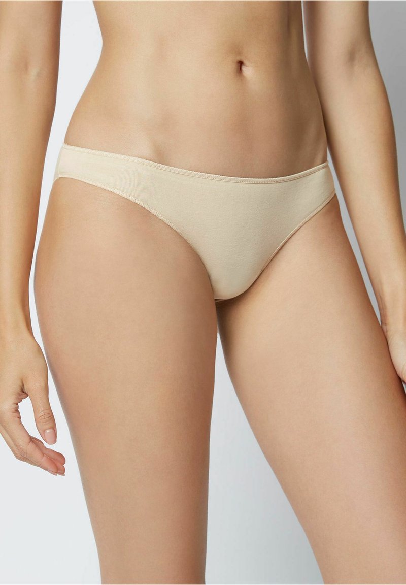 Chiloți bikini din bumbac bej, cu o textură netedă, design cu talie joasă și acoperire minimă pe laterale, având detalii de cusătură vizibile.