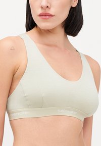 Sutiã desportivo verde claro, feito de material suave, apresentando um decote em forma de colher e uma faixa de suporte com o logótipo "icebreaker" na bainha.