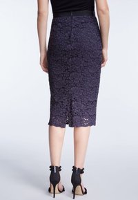 Krajková tužková sukně v tmavě fialové barvě s květinovým vzorem, ke kolenům, s rozparkem vzadu a černým pasem. V kombinaci s černými podpatky.