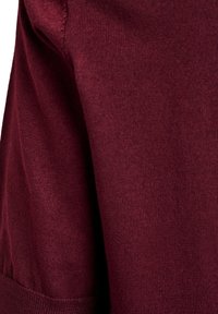 Bordeauxfarbenes Strickgewebe mit glatter Textur, zeigt die Naht am Ärmel und die Manschettendetails. Nahaufnahme, die Farbe und Material hervorhebt.