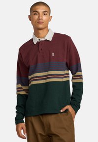 Polo de manga larga en color burdeos, verde y beige con rayas horizontales. Presenta un cuello blanco, tapeta de botones y un logo en el pecho.