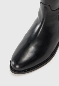 Bota de piel negra hasta el tobillo con punta afilada, textura suave, costuras mínimas y tacón redondeado. Sin herrajes visibles ni adornos.