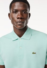 Polo in verde menta chiaro, con colletto a tre bottoni e piccolo logo di coccodrillo ricamato sul petto. Tessuto texture.