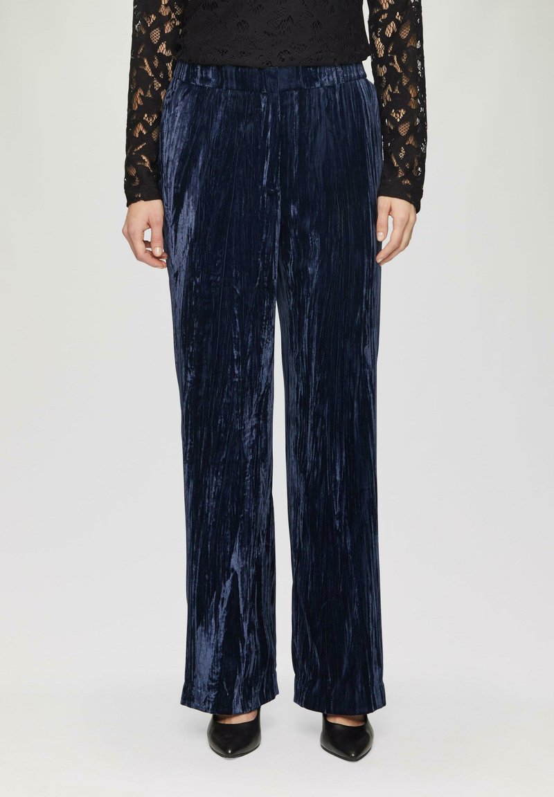 Marineblauwe fluwelen broek met wijde pijpen, voorzien van een gestructureerde afwerking en een elastische tailleband, gecombineerd met zwarte schoenen en een lange mouw van kant.