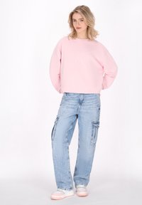 Sweatshirt cropped rosa con stampa "SOFT", abbinato a jeans cargo blu chiaro con tasche. Indossato con sneakers nei colori pastello.