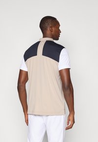 Camisa polo masculina com um corpo bege, yoke preto, mangas brancas e um colarinho curto com um logo discreto nas costas. Textura suave.