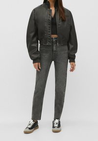 Chaqueta bomber negra corta con puños acanalados, combinada con jeans altos grises y zapatillas negras con cordones blancos y detalles grises.