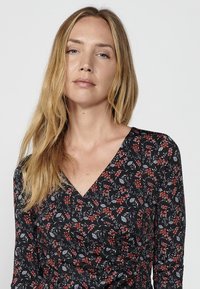 Schwarzes Wickelkleid mit floralem Muster in Rot, Weiß und Grün. Es hat einen V-Ausschnitt und lange Ärmel und besteht aus einem weichen, strukturierten Stoff.