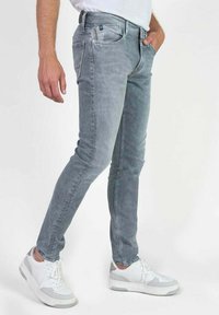 Jeans gris délavé avec une coupe slim, dotés de cinq poches et d'une couture contrastante. Associés à des baskets blanches avec des accents gris.