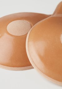 Nude silikonowe miseczki biustonosza o gładkim, błyszczącym wykończeniu i miękkiej, cienkiej krawędzi z tkaniny. Każda miseczka ma okrągłe, wypukłe centrum zapewniające wsparcie.