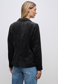 Černá kordurová sako s klopovým límcem, textured povrch, přiléhavý střih a dlouhými rukávy, spárované se světle modrými džíny.