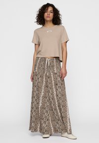Beige crop top met een klein logo, gecombineerd met een lange rok in bruin slangenpatroon met een trekkoord in de taille en een gladde textuur.