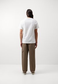 Hvid bomuld t-shirt med klassisk rund hals, parret med brune cargo bukser med sidelommer og en afslappet pasform. Enkel design, ingen logoer.