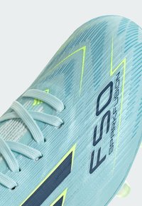 Chaussure de football bleu clair avec surface texturée, lacets bleu clair, accents jaunes et "F50 Spark Fusion" imprimé en noir sur le côté.
