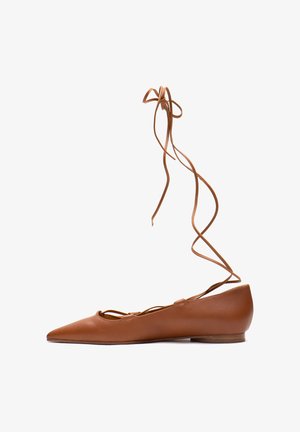 Chaussure ballerine plate en cuir marron avec bout pointu et longs lacets à nouer autour de la cheville sur fond blanc.