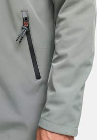 Helle graue, wasserdichte Jacke mit einer Reißverschlusstasche mit schwarzem Besatz und Kordeldetail, glatte Textur und taillierte Passform.