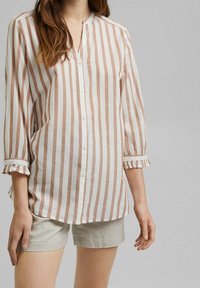 Chemise à rayures couleur crème et marron clair, avec des manches trois-quarts et des poignets volantés. Tissu léger, coupe décontractée.