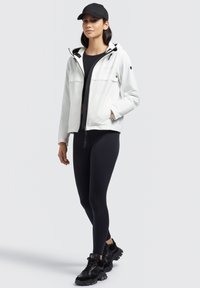 Veste blanche zippée avec capuche, accents noirs et deux poches avant. Associée à des leggings noirs et des baskets noires chunky.