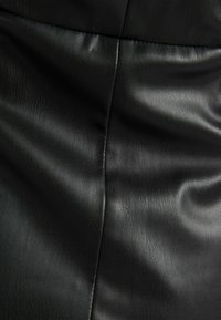 Slät svart läder tyg med synlig söm som går vertikalt ner i mitten, visar subtila rynkor och textur.