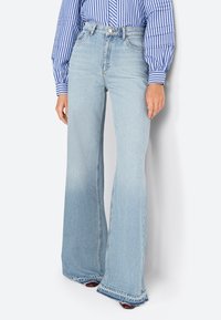 Jean évasé bleu clair en denim, avec une taille haute, une texture légèrement décolorée et un ourlet brut en bas.